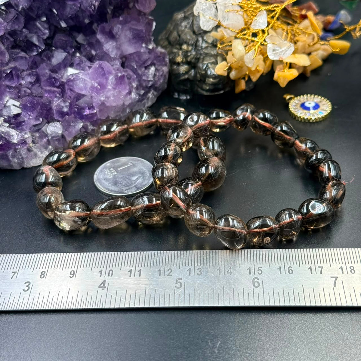 Smoky quartz tumble bracelet shown from above beside amethyst crystal and charms