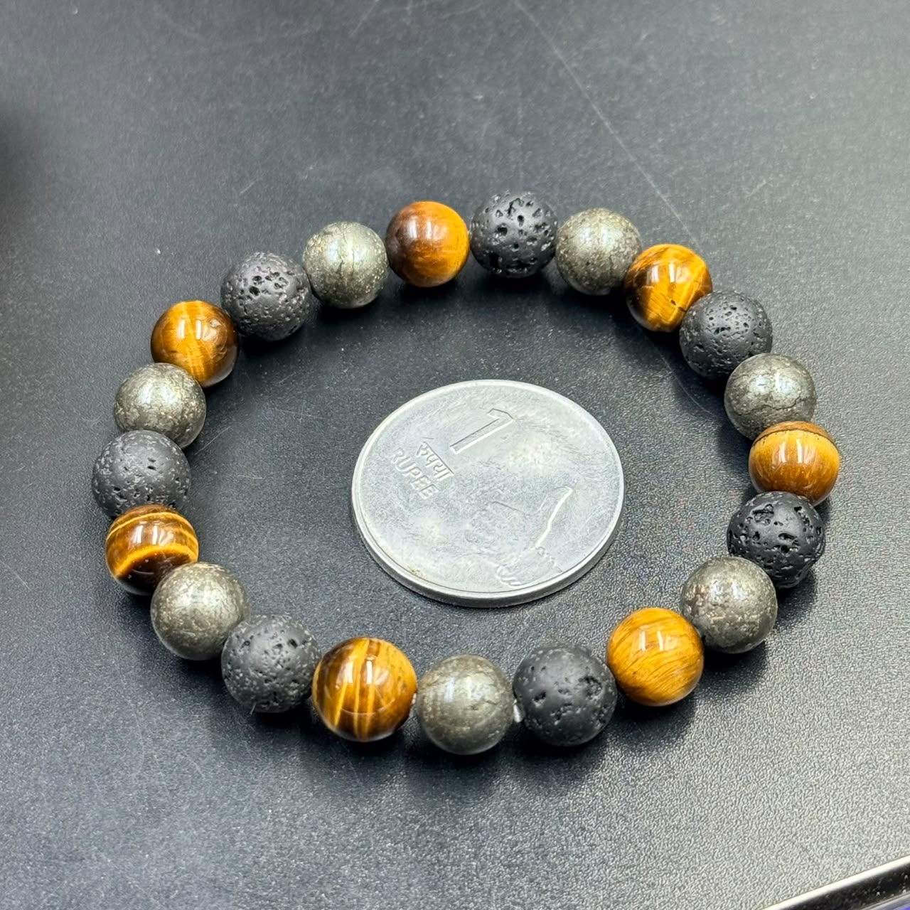 Success Shield bracelet with orange tiger-eye and metallic lava beads on dark gray background