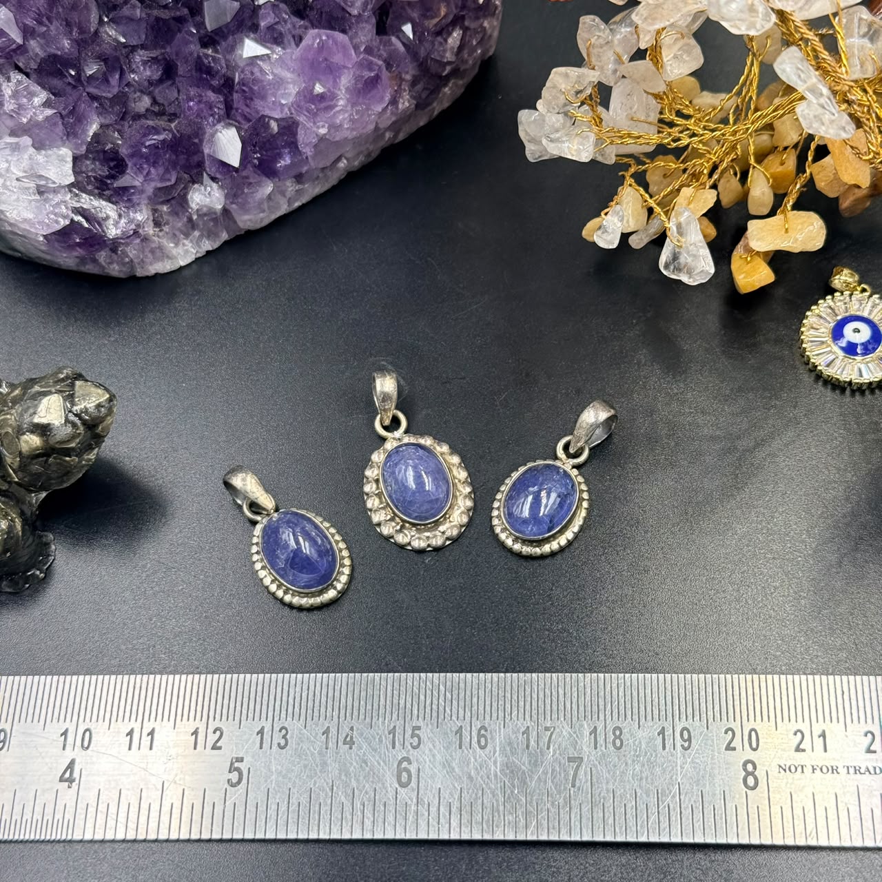 Three oval blue gemstone locket pendants in 925 silver with bail on black background and ruler