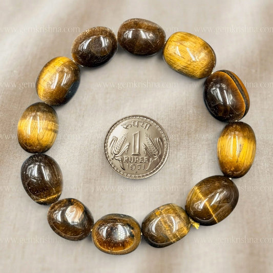 Tiger eye tumble bracelet close-up with rounded beads and rupee coin for size on light background