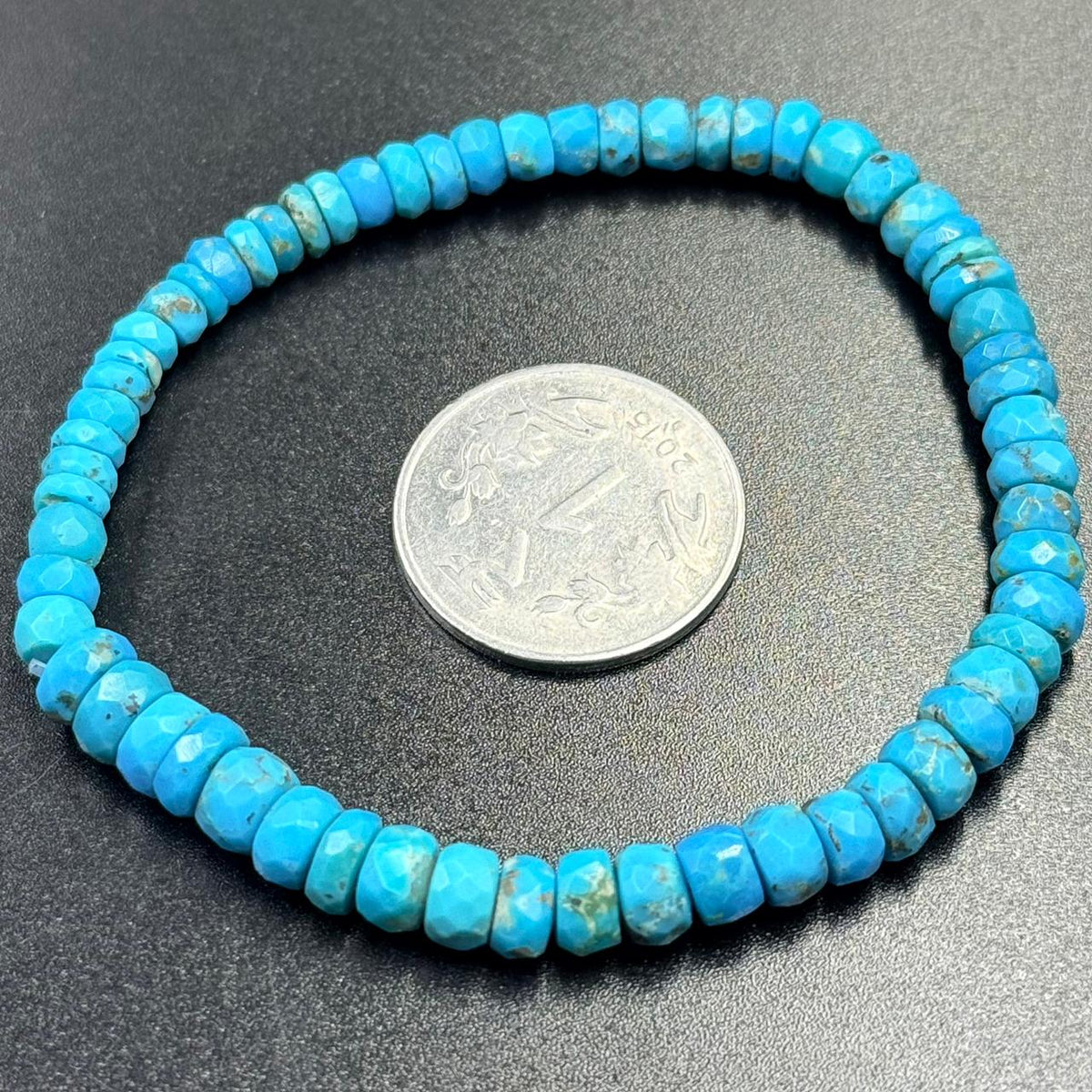 Turquoise flat rondelle beads bracelet loop with coin for scale on dark background