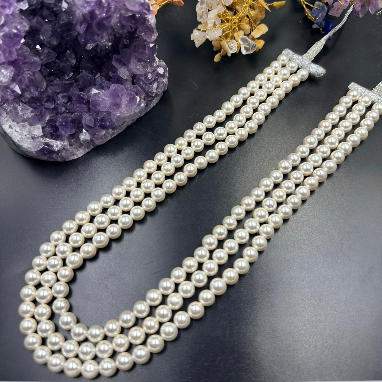 White pearl 3-layer mala necklace with silk tassel on dark display, close-up view