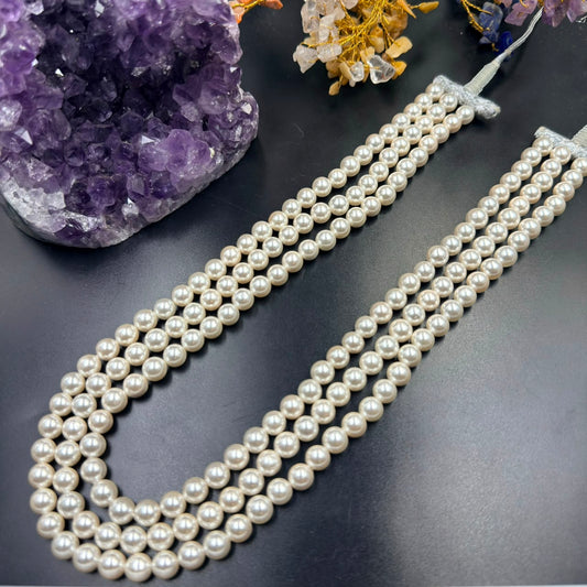 White pearl 3-layer mala necklace with silk tassel on dark display, close-up view