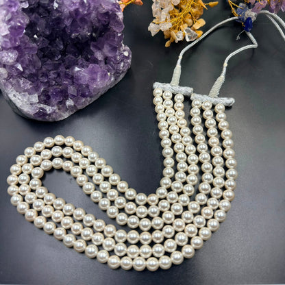 White pearl 3-layer mala necklace laid flat with tassel strings over dark background