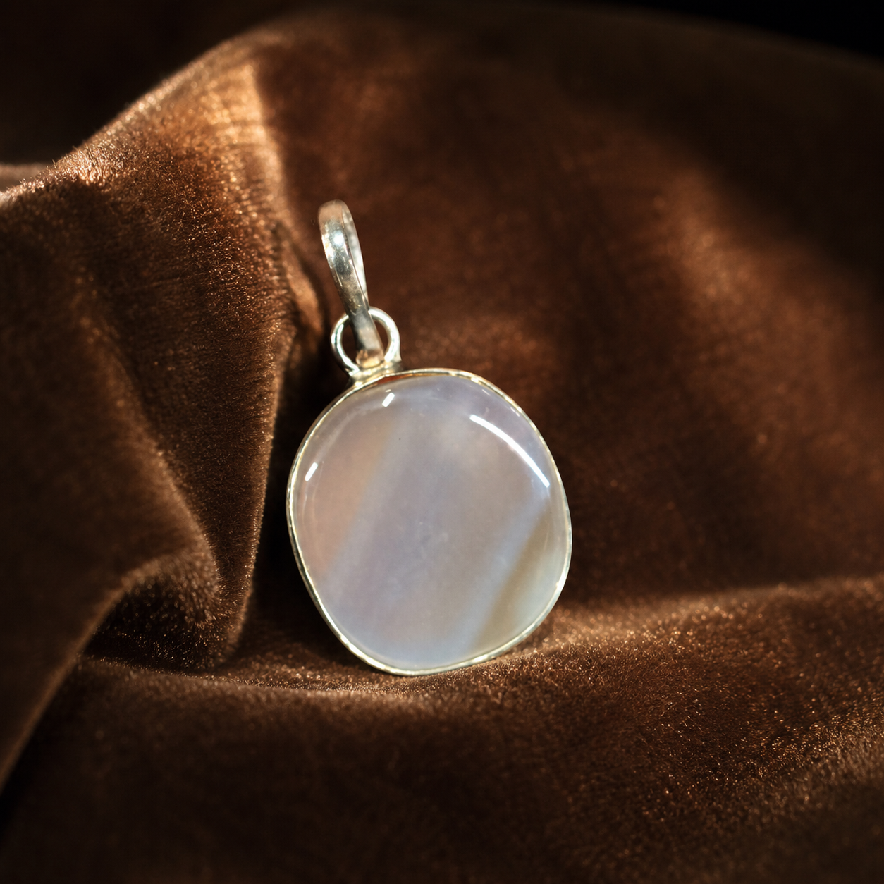 White Sulemani agate locket pendant with oval stone and silver-toned bail on brown fabric