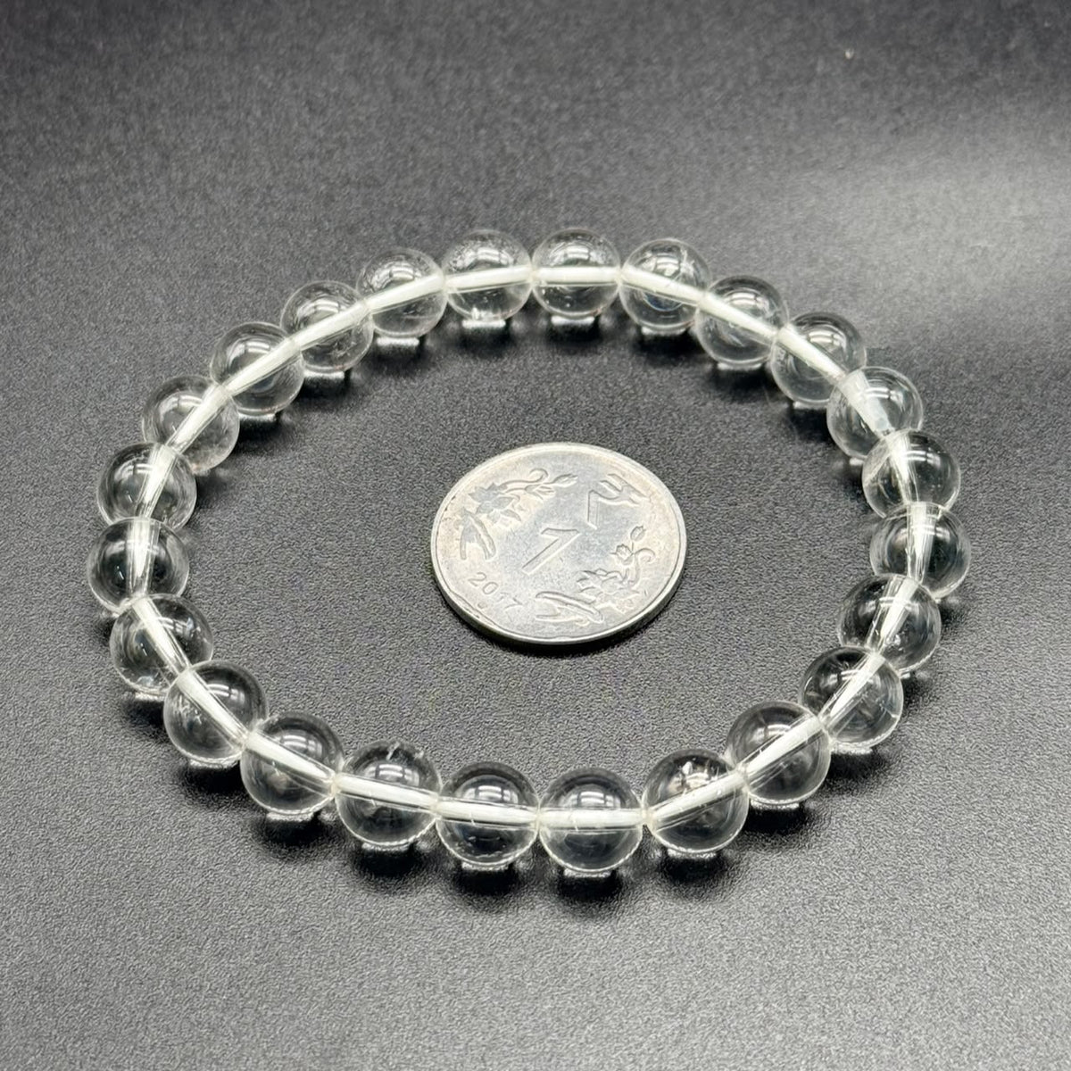 White topaz beaded bracelet close-up showing round clear stones on gray background with coin