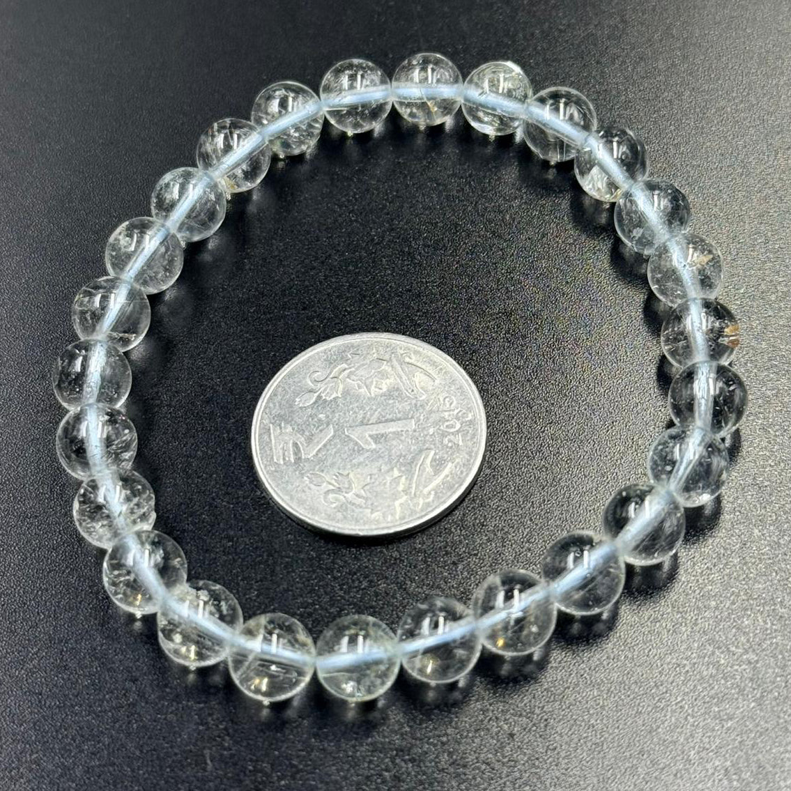 White topaz beaded bracelet close-up with round clear stones on dark fabric with coin for size
