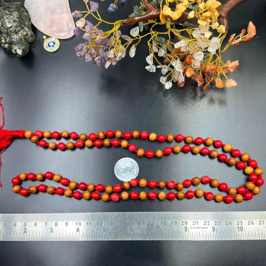 Wood and coral Jaap mala necklace beads with red tassel and coin for scale on gray surface