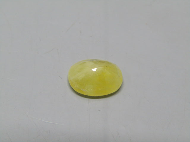 Yellow sapphire pukhraj oval cabochon gemstone with glossy dome on plain gray surface