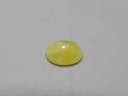 Yellow sapphire pukhraj oval cabochon gemstone with glossy dome on plain gray surface