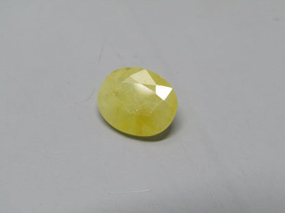 Yellow sapphire pukhraj oval gemstone cabochon with bright reflective facets on gray background