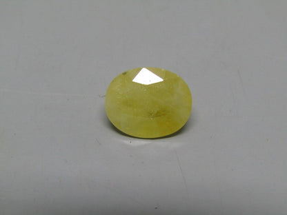 Yellow sapphire pukhraj gemstone oval cabochon with faceted top view on gray surface