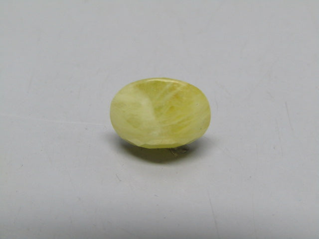 Yellow sapphire pukhraj oval cabochon gemstone showing smooth domed shape on gray surface