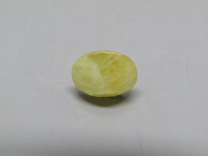Yellow sapphire pukhraj oval cabochon gemstone showing smooth domed shape on gray surface